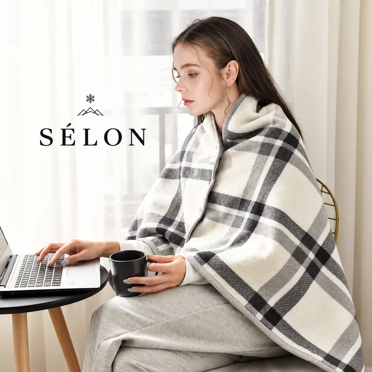 Woman working at a desk wrapped in the cream check flannel shawl, holding a mug